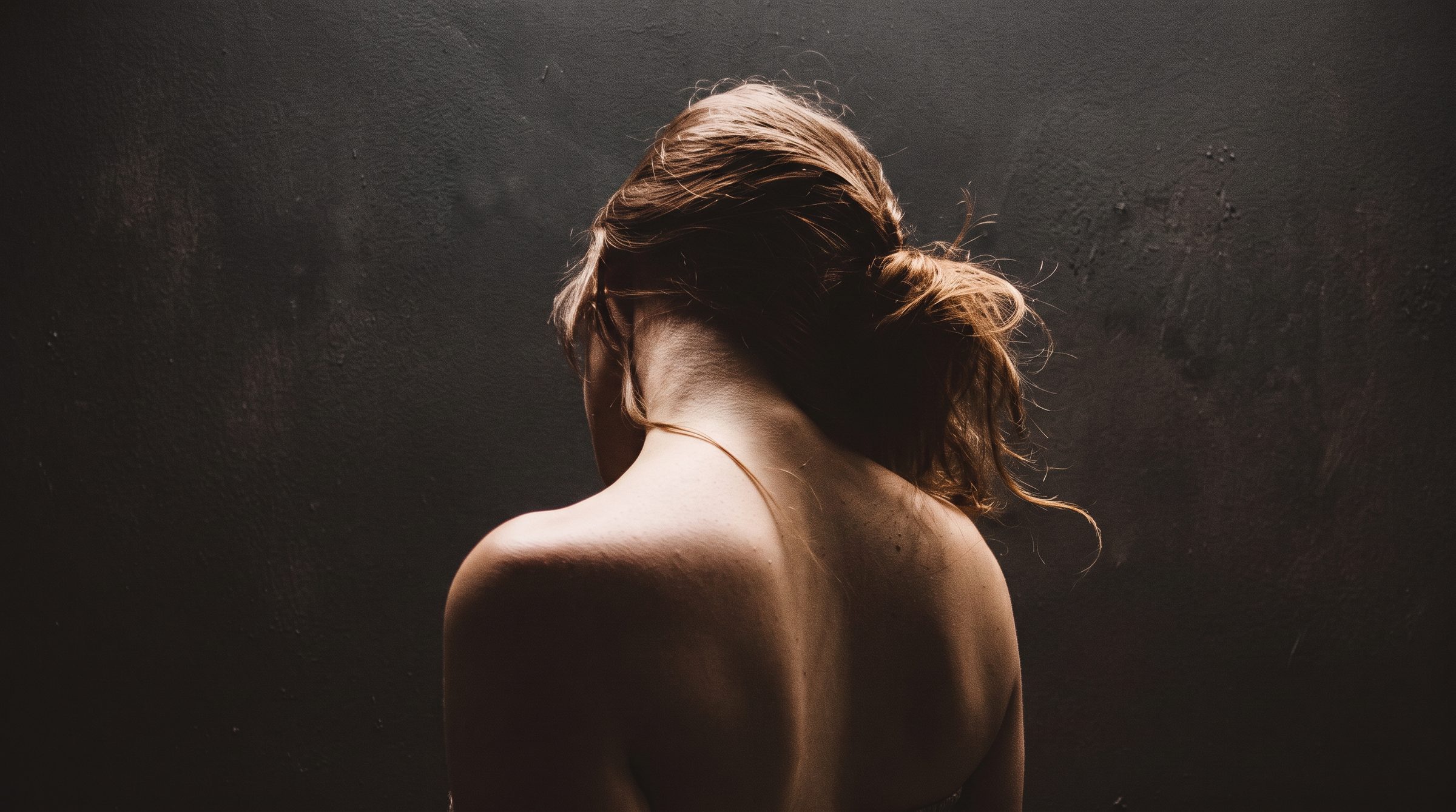 Woman seen from behind in soft dramatic light, hair gathered, bare shoulders
